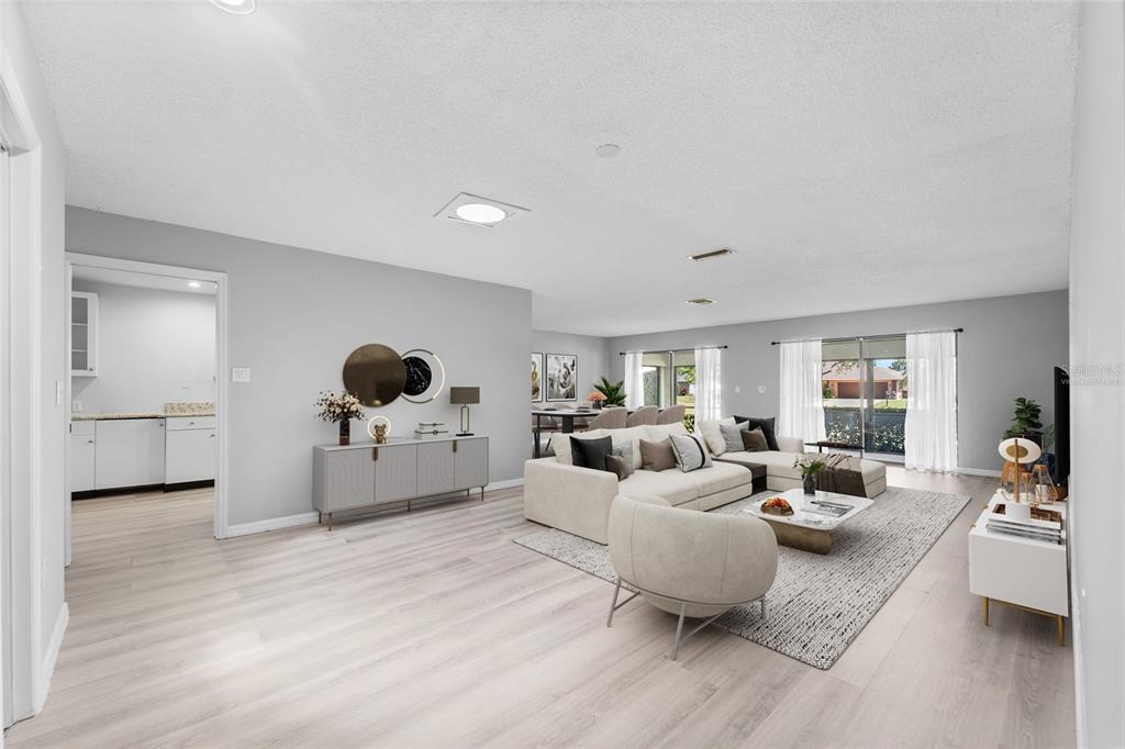 A spacious, open-concept living room features light wood flooring, a sectional sofa, and neutral decor — 3766 BALLANTRAE DRIVE UNIT 22D, SARASOTA, FL