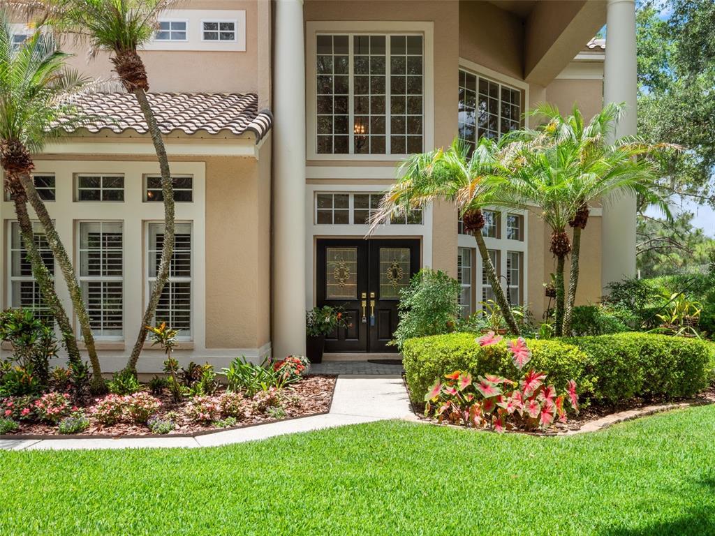 The exterior of a two-story home features a columned entryway, double doors, and landscaping — 17422 HEATHER OAKS PLACE, TAMPA, FL