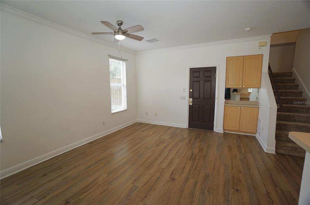 An empty room features wood-look flooring, a ceiling fan, a dark door, and a staircase — 101 KEY HAVEN COURT UNIT 1, TAMPA, FL