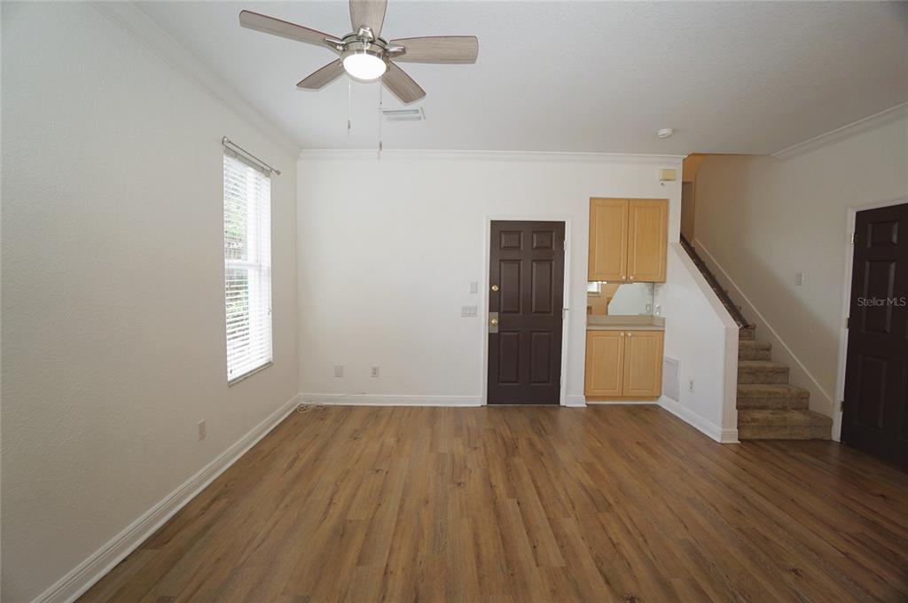 An empty room features wood-look flooring, a ceiling fan, a dark door, and a staircase — 101 KEY HAVEN COURT UNIT 1, TAMPA, FL