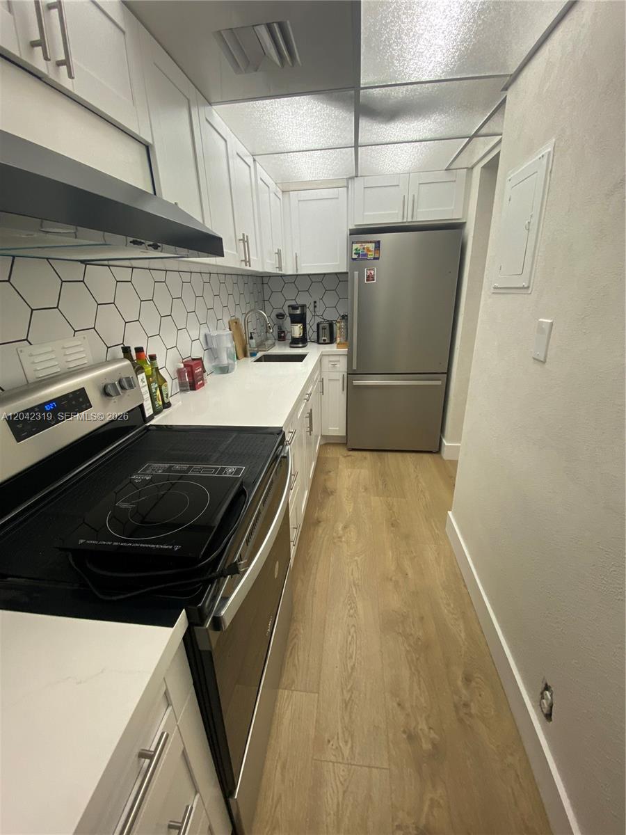 A galley kitchen features white cabinets, stainless steel appliances, and a hexagonal tile backsplash — 1000 West Avenue # 531, Miami Beach FL 33139, MIAMI BEACH, FL