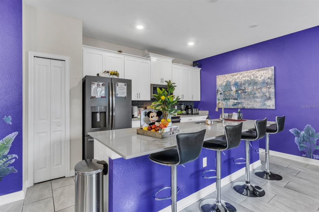 A kitchen features white cabinets, a gray quartz island with bar seating, and purple walls — 4815 S LOVE STOREY LANE, KISSIMMEE, FL