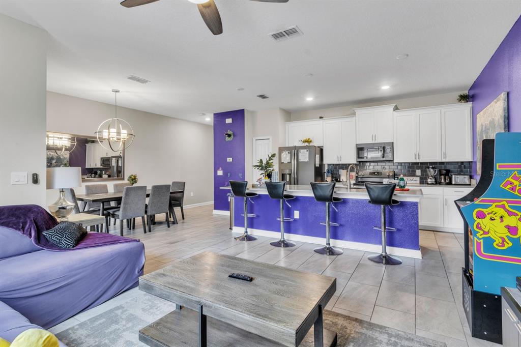 An open-concept kitchen and living area features a purple island, white cabinets, and tile flooring — 4815 S LOVE STOREY LANE, KISSIMMEE, FL