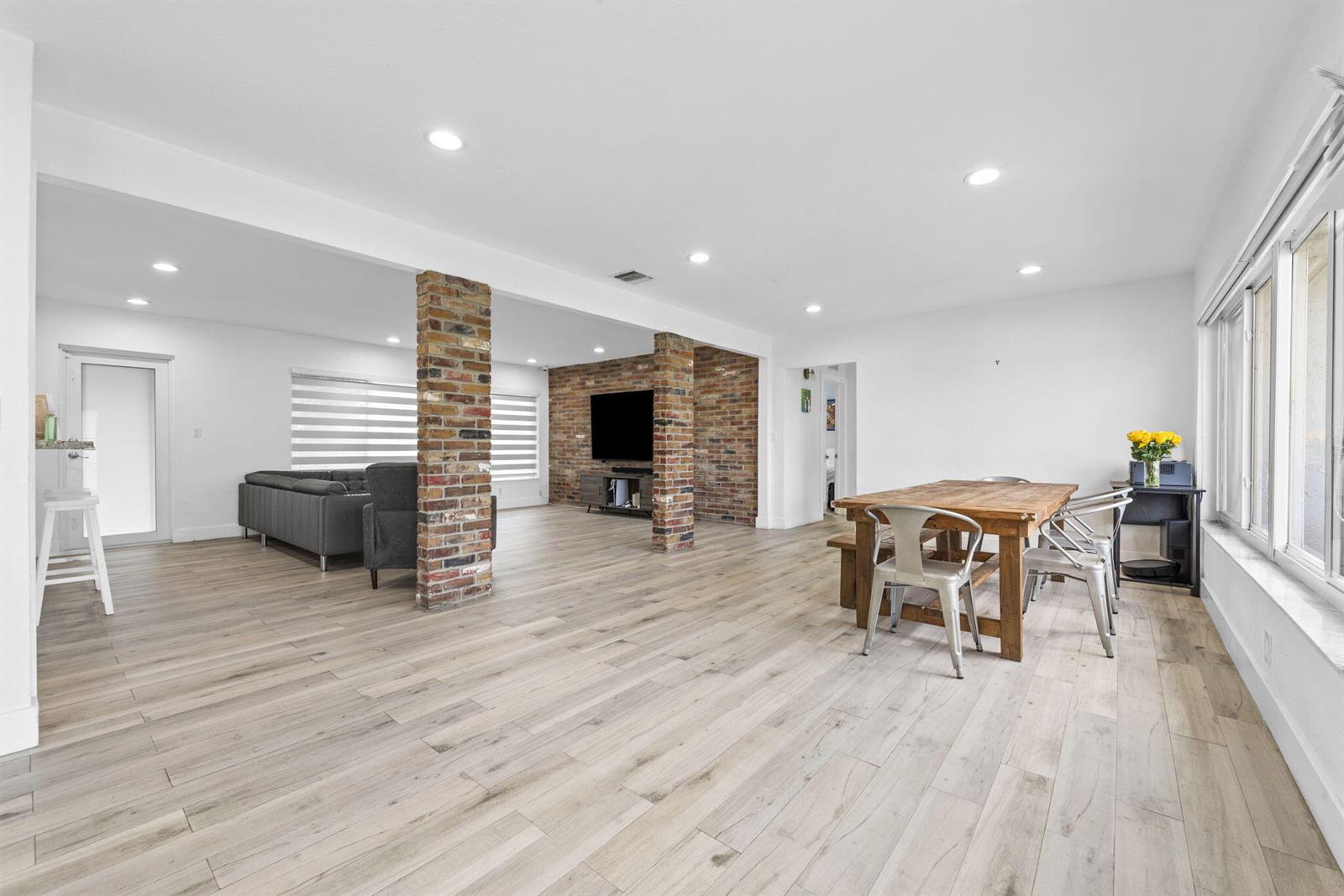 An open-concept living and dining area features light wood flooring and two exposed brick columns — 409 N 14th Avenue, Hollywood FL 33020, HOLLYWOOD, FL