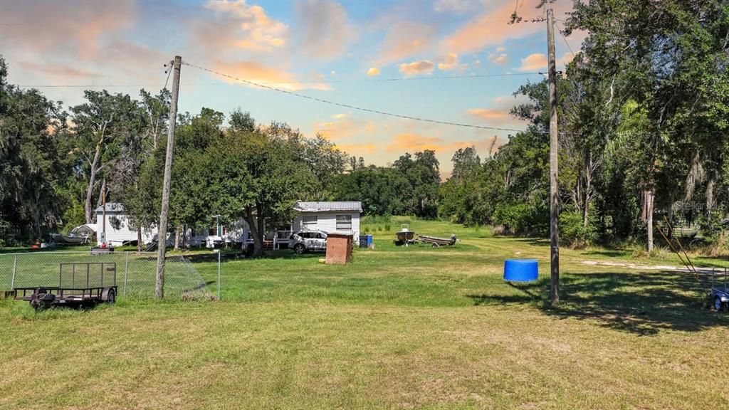 A grassy yard features a small house, a utility trailer, and a blue barrel — 5606 WATSON ROAD, RIVERVIEW, FL