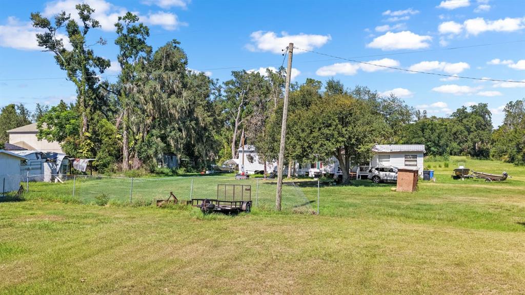 A grassy backyard features a chain-link fence, a utility trailer, and a small white house — 5606 WATSON ROAD, RIVERVIEW, FL