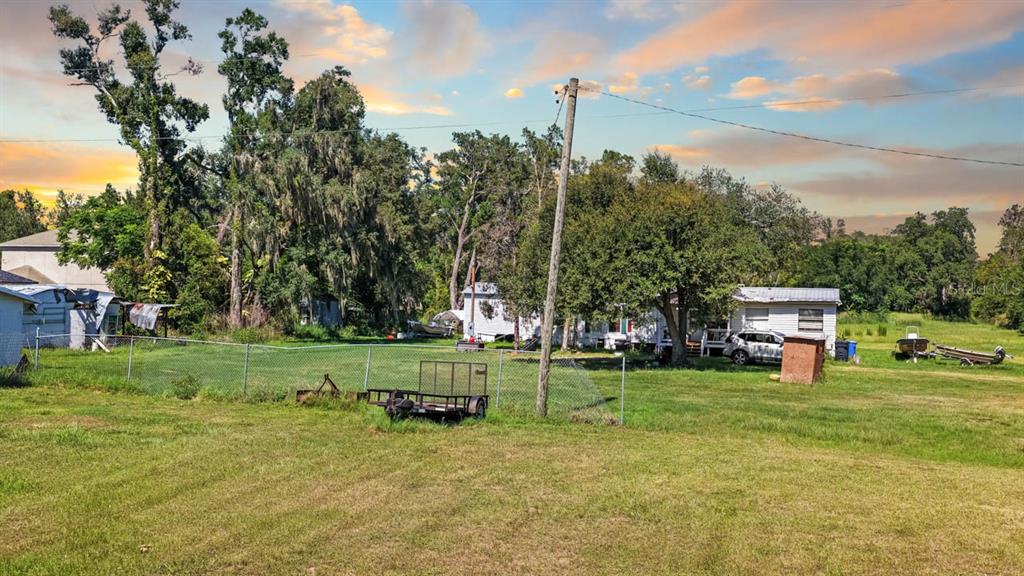 A grassy yard features a chain-link fence, a utility trailer, and a small white house — 5606 WATSON ROAD, RIVERVIEW, FL