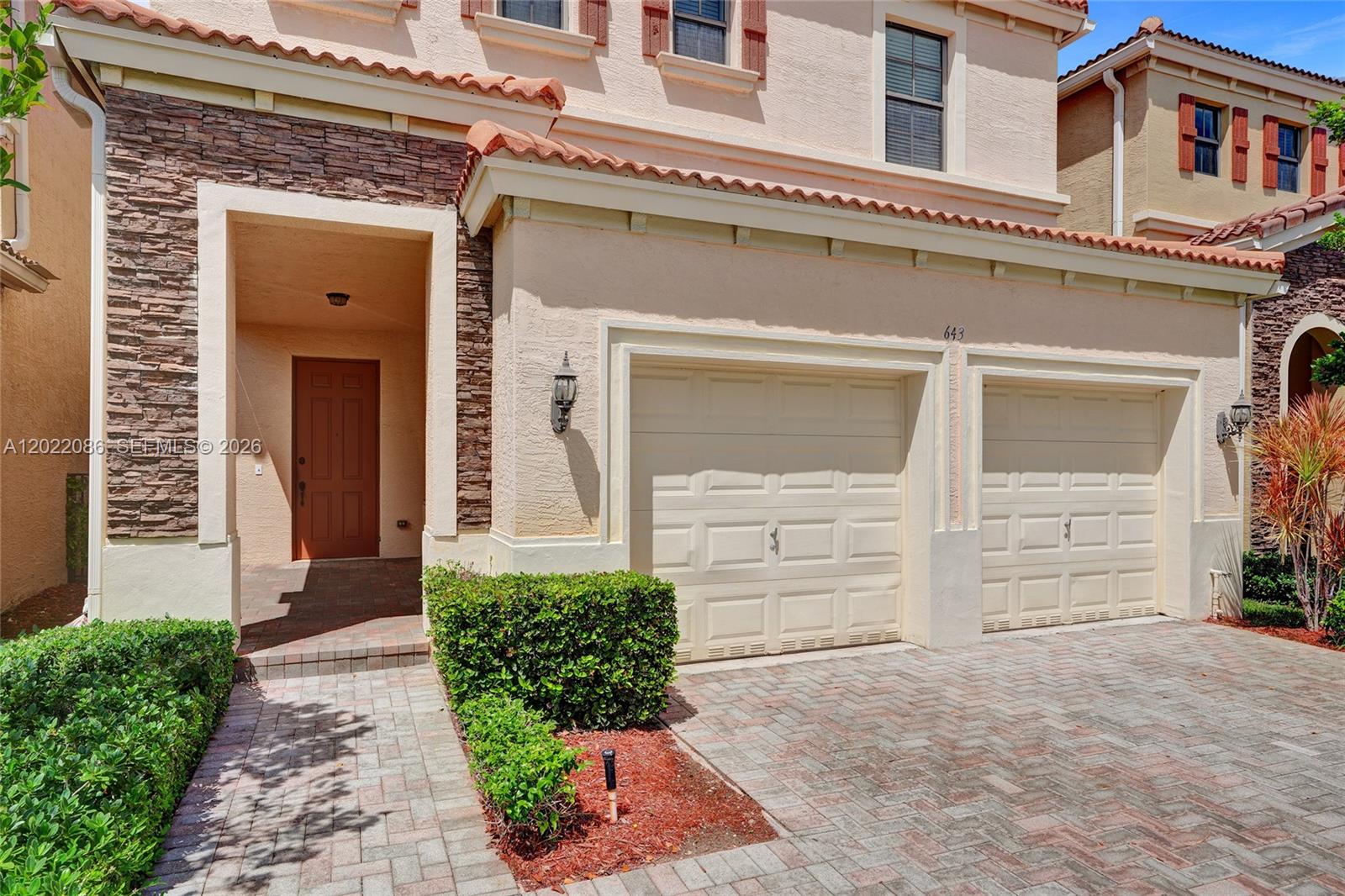 A two-story house exterior features a stone-accented entrance, two garage doors, and a paved driveway — 643 NE 191st Ter, Miami FL 33179, MIAMI, FL