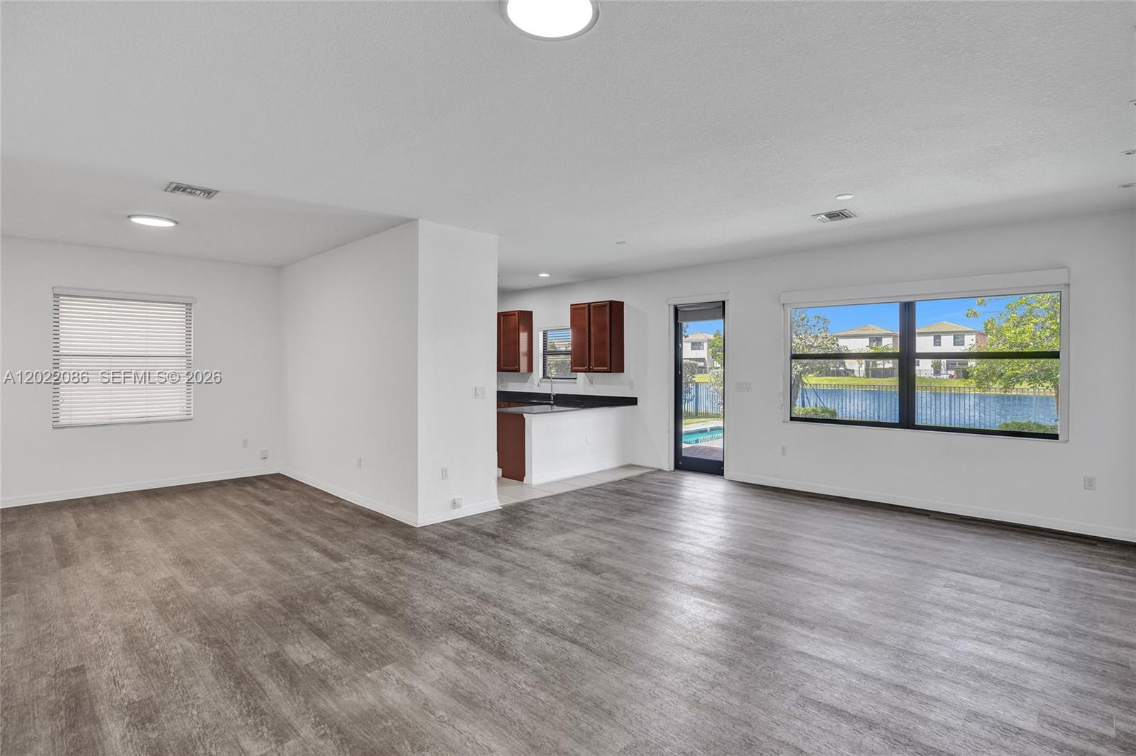 An open-concept living area features wood-look flooring, white walls, and a view of a lake — 643 NE 191st Ter, Miami FL 33179, MIAMI, FL