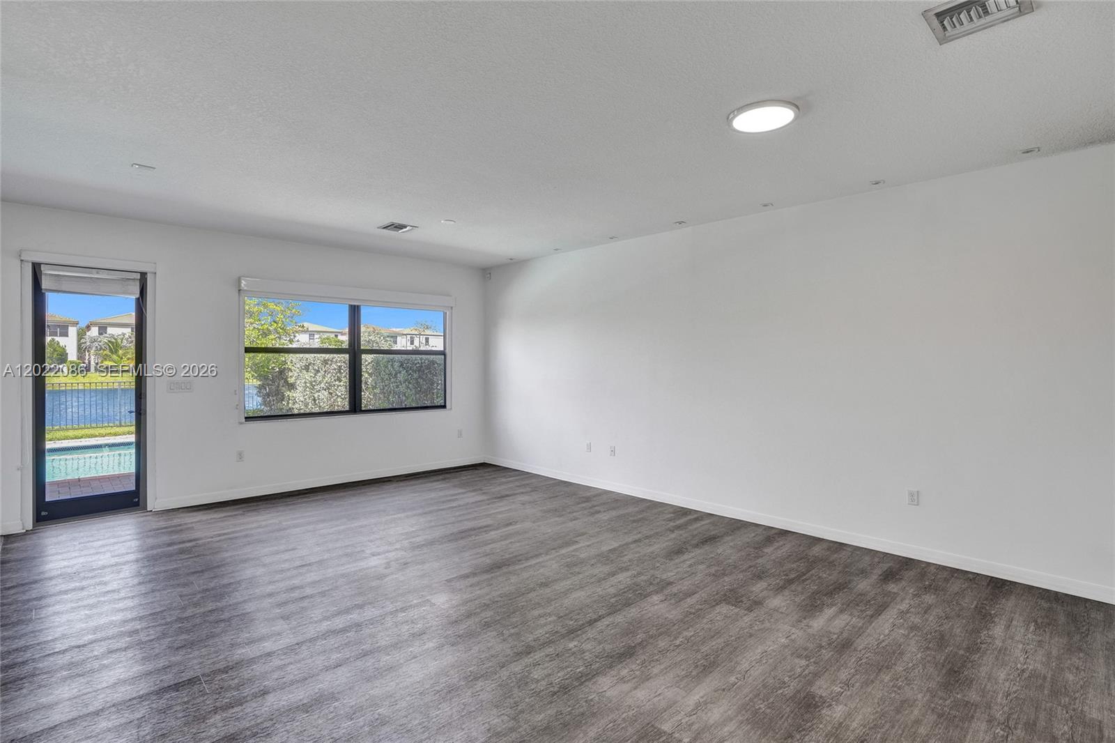 An empty room features gray wood-look flooring, white walls, recessed lighting, and a sliding glass door — 643 NE 191st Ter, Miami FL 33179, MIAMI, FL