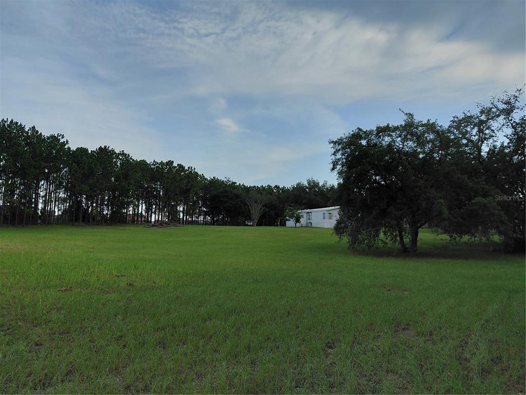 A large grassy field with a mobile home in the distance and surrounding trees — 14240 LOST LAKE ROAD, CLERMONT, FL