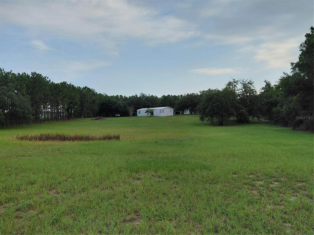 A white mobile home sits in the distance on a large, grassy, tree-lined lot — 14240 LOST LAKE ROAD, CLERMONT, FL