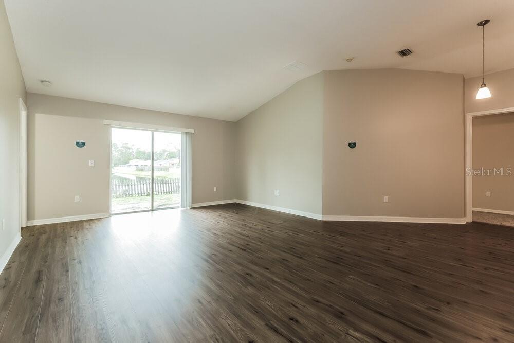 An empty living room features wood-look flooring, light gray walls, and a sliding glass door — 6415 BUCKHEAD COURT, WESLEY CHAPEL, FL