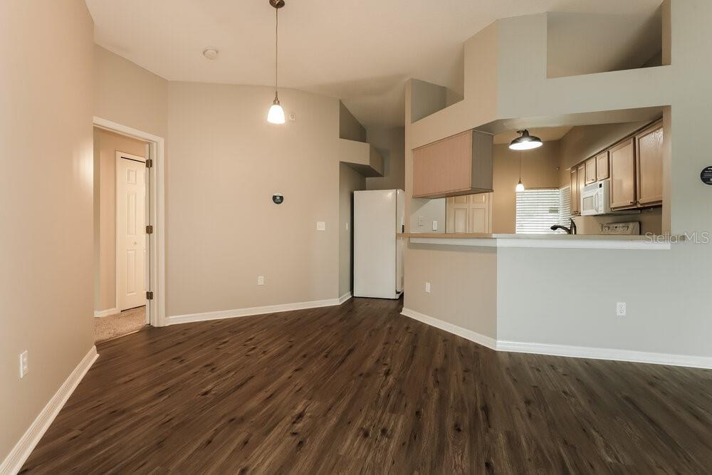 An open-concept dining area with wood-look flooring leads into a kitchen with a breakfast bar — 6415 BUCKHEAD COURT, WESLEY CHAPEL, FL
