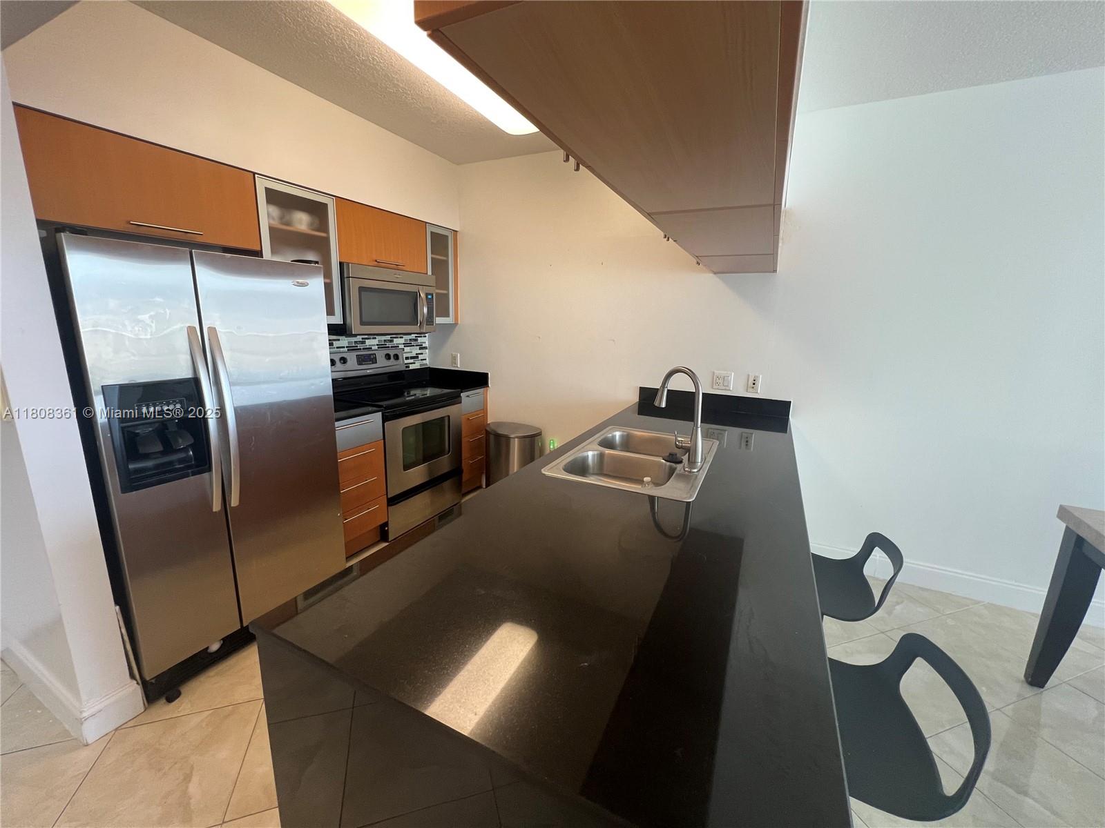A kitchen features stainless steel appliances, wood cabinets, and a black countertop island with seating — 1750 N Bayshore Dr # 1410, Miami FL 33132, MIAMI, FL