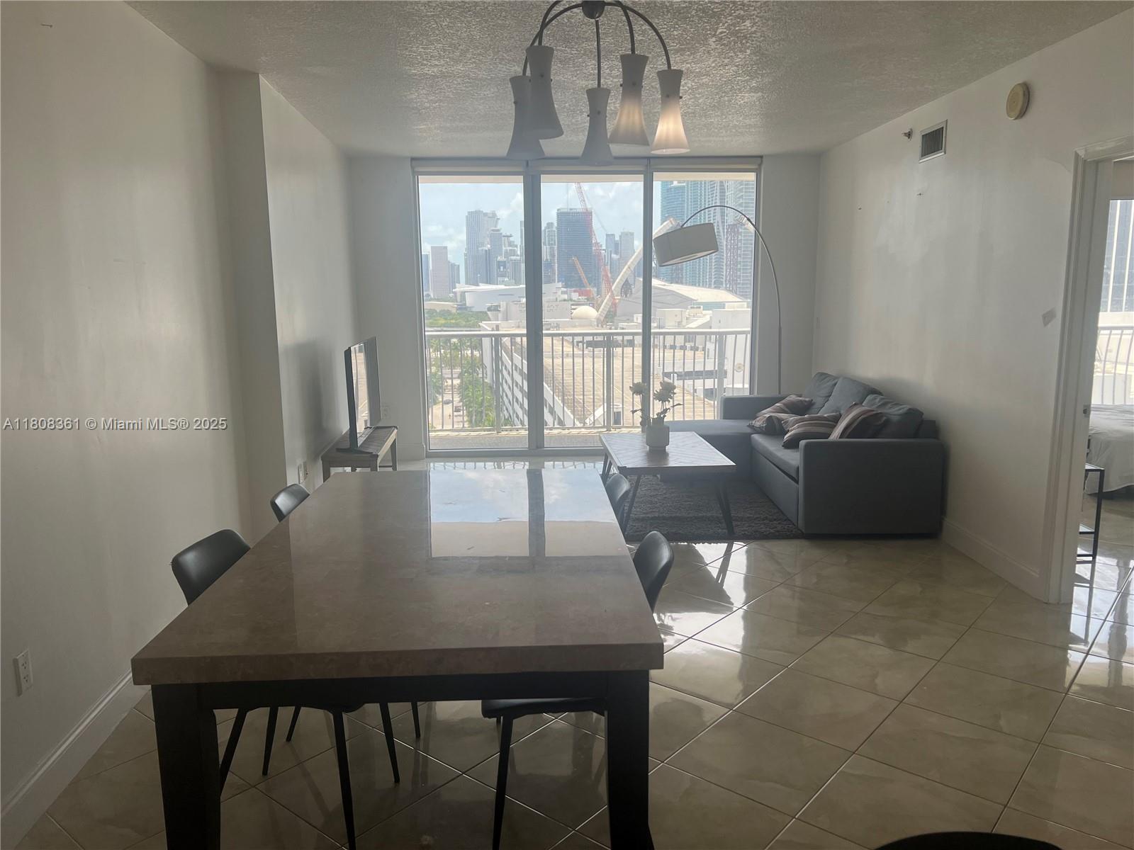 A dining area and living room with tile floors overlook a city skyline through windows — 1750 N Bayshore Dr # 1410, Miami FL 33132, MIAMI, FL