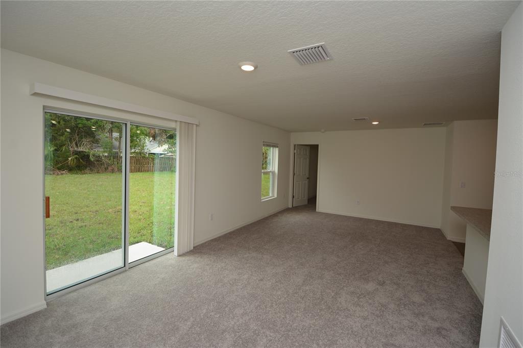 An empty living room with gray carpet, white walls, and a sliding glass door — 38 BALTIMORE LANE, PALM COAST, FL