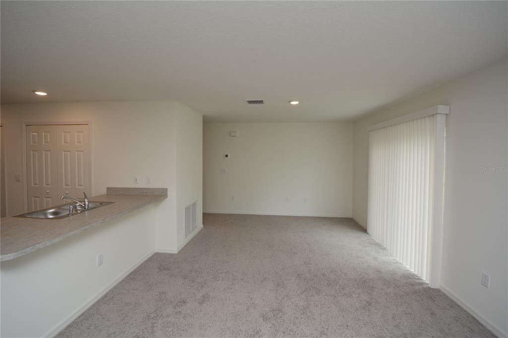 An open-concept living area features gray carpeting, a kitchen breakfast bar, and sliding glass doors — 38 BALTIMORE LANE, PALM COAST, FL