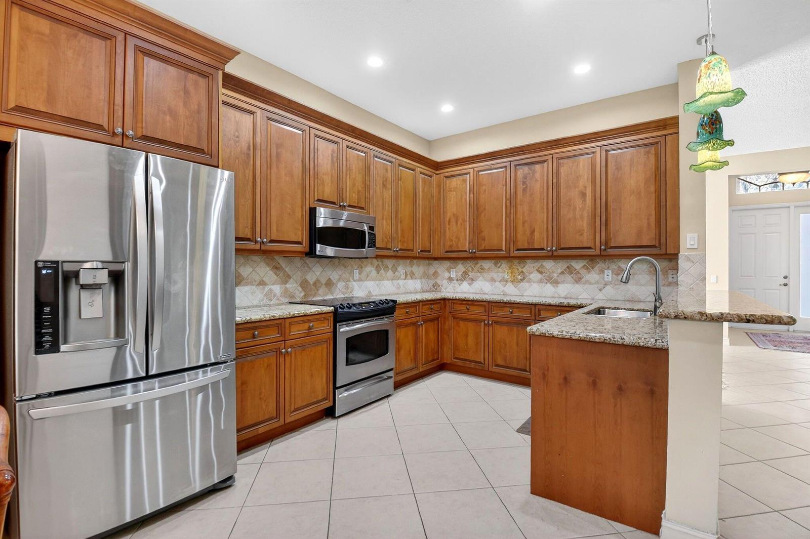 A kitchen features wood cabinets, granite countertops, stainless steel appliances, and a tiled backsplash — 7420 Twin Falls Drive, Boynton Beach FL 33437, BOYNTON BEACH, FL