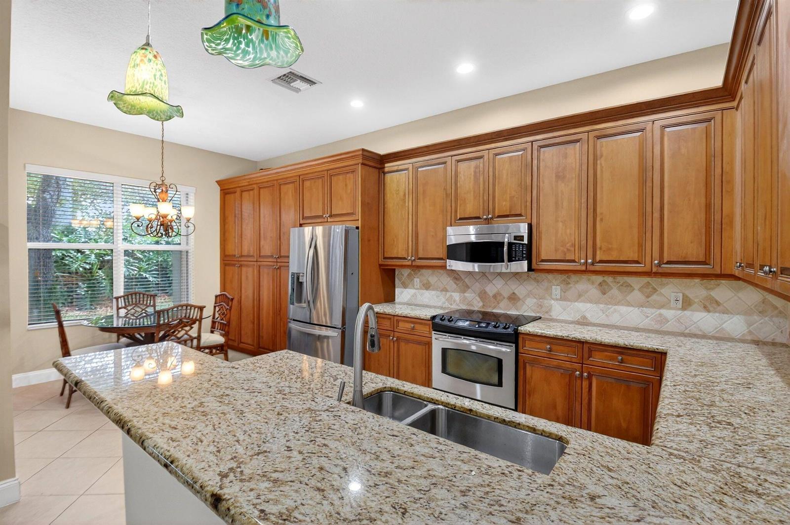 A kitchen features wood cabinets, granite countertops, stainless steel appliances, and a dining area — 7420 Twin Falls Drive, Boynton Beach FL 33437, BOYNTON BEACH, FL