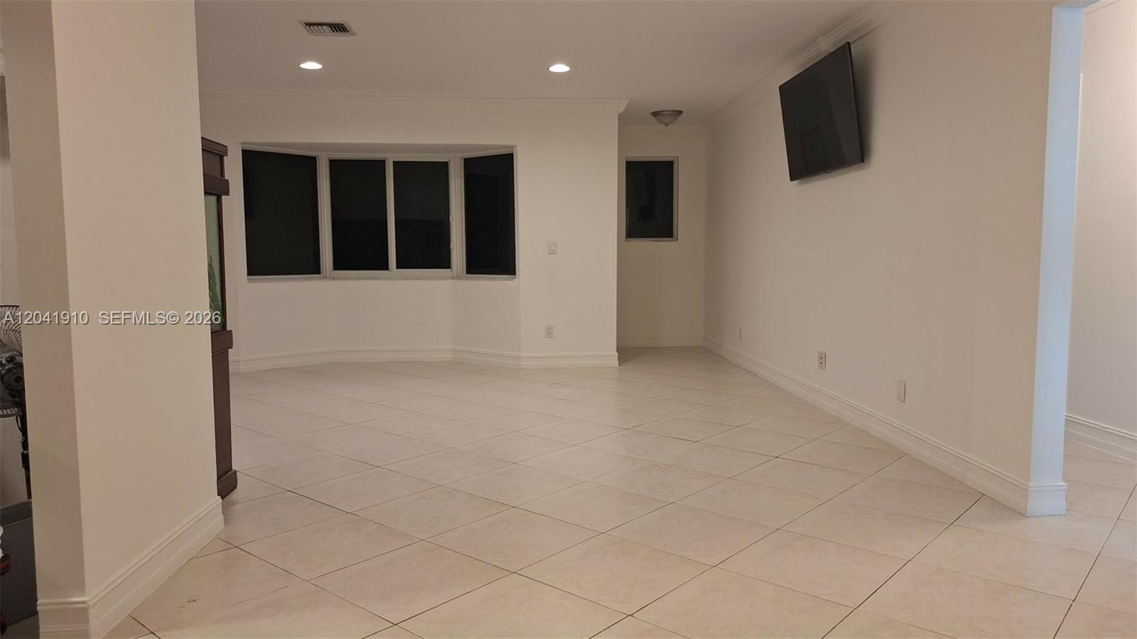 A spacious, empty room features white walls, tile flooring, a bay window, and a wall-mounted television — 1800 N 55th Ave, Hollywood FL 33021, HOLLYWOOD, FL