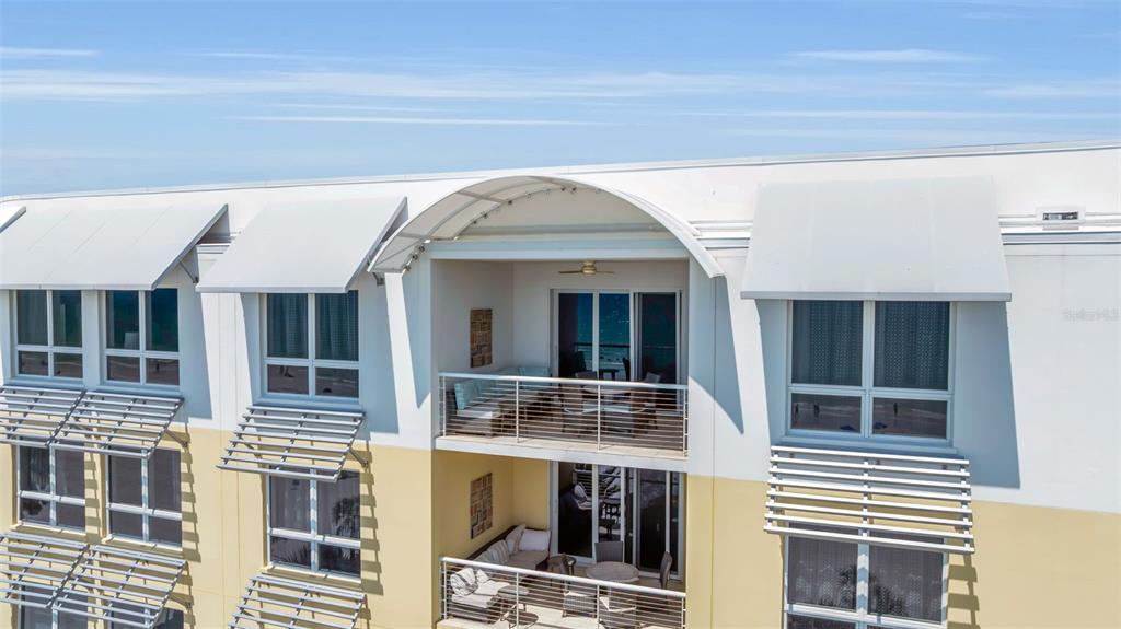 An exterior view of a multi-story building featuring balconies with outdoor furniture and metal awnings — 915 SEASIDE DRIVE UNIT 611, SARASOTA, FL