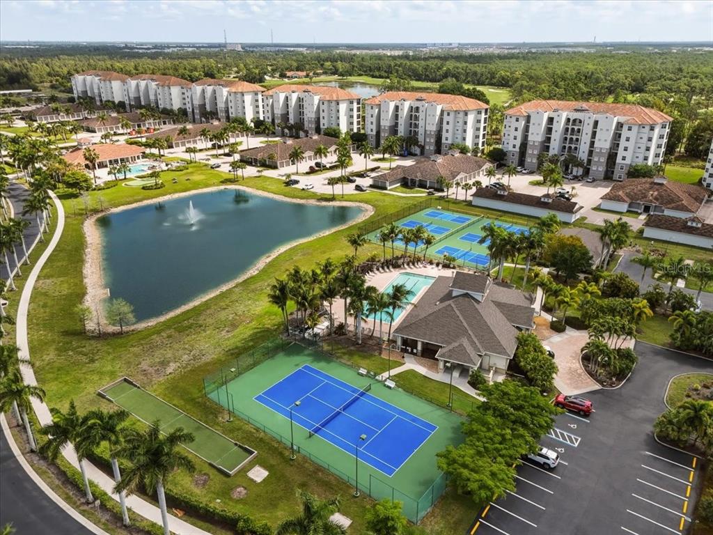 An aerial view shows a residential complex with a pool, tennis courts, and a pond — 4223 LIRON AVENUE UNIT 104, FORT MYERS, FL
