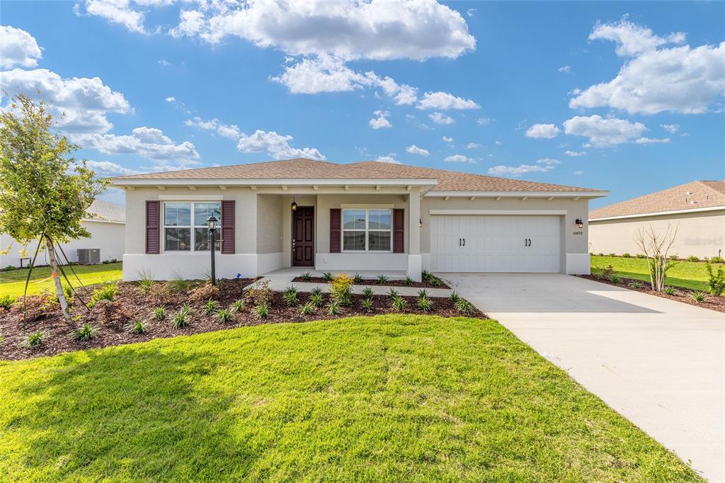 A single-story house with a beige stucco exterior, a two-car garage, and a front lawn — 10693 SW 102ND LANE, OCALA, FL