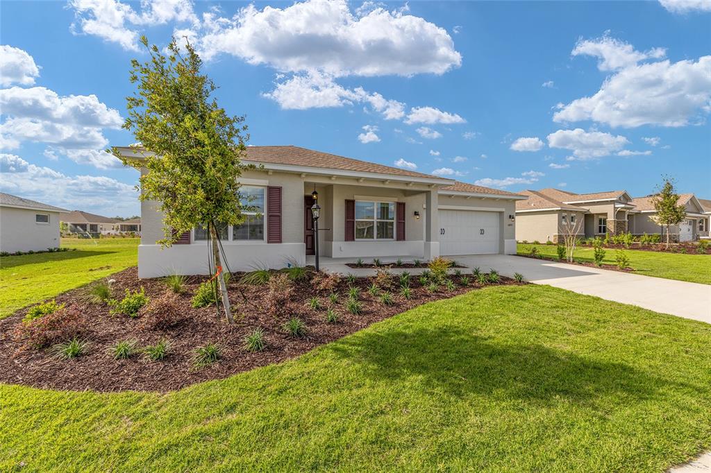 A single-story suburban house with a tan stucco exterior, a two-car garage, and landscaped yard — 10693 SW 102ND LANE, OCALA, FL