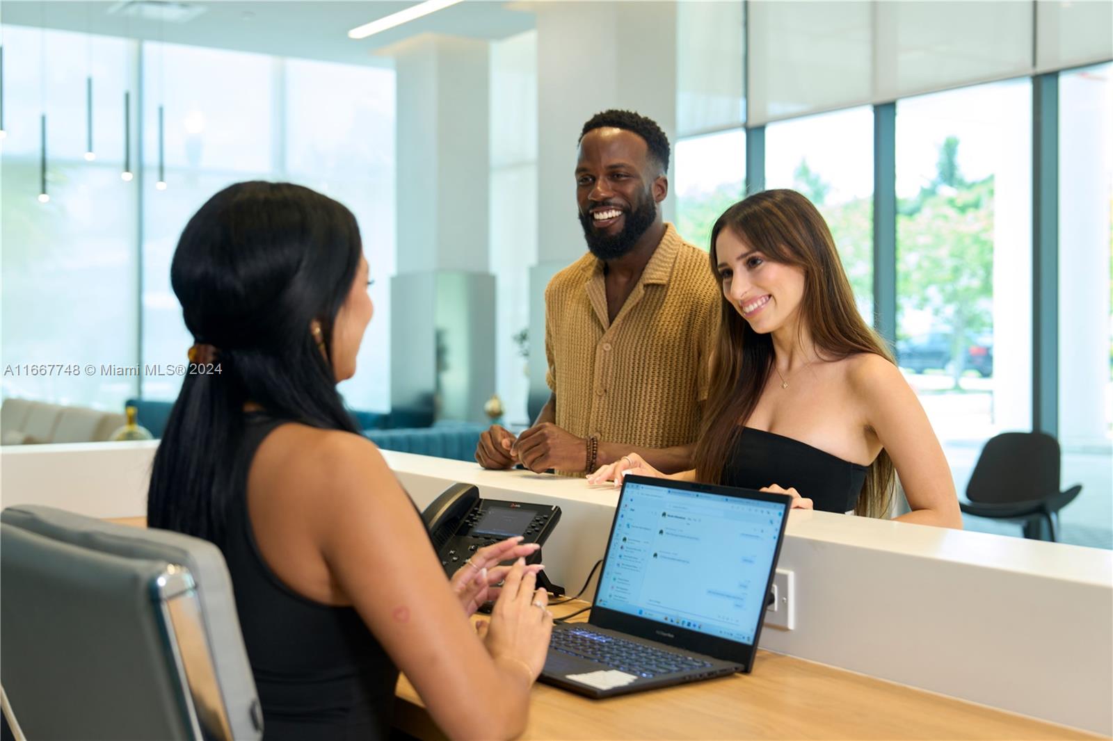 A receptionist assists a couple at a modern building's front desk with a laptop — 1809 Jackson St # 1002, Hollywood FL 33020, HOLLYWOOD, FL