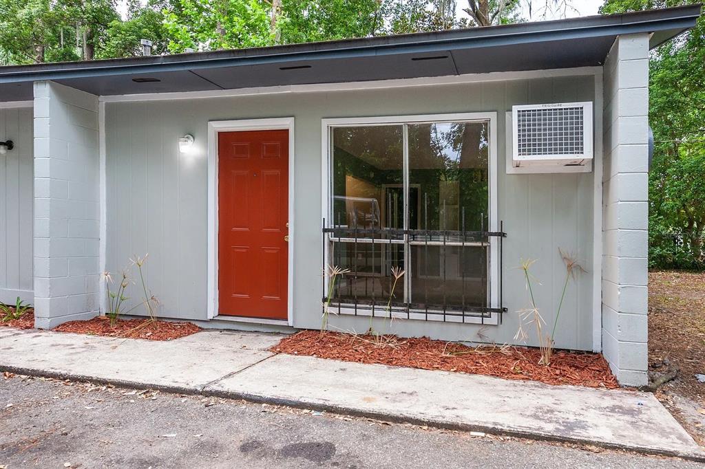 The exterior of a single-story unit features a red door, a window with security bars, and an air conditioner — 409 NE 11TH STREET, GAINESVILLE, FL