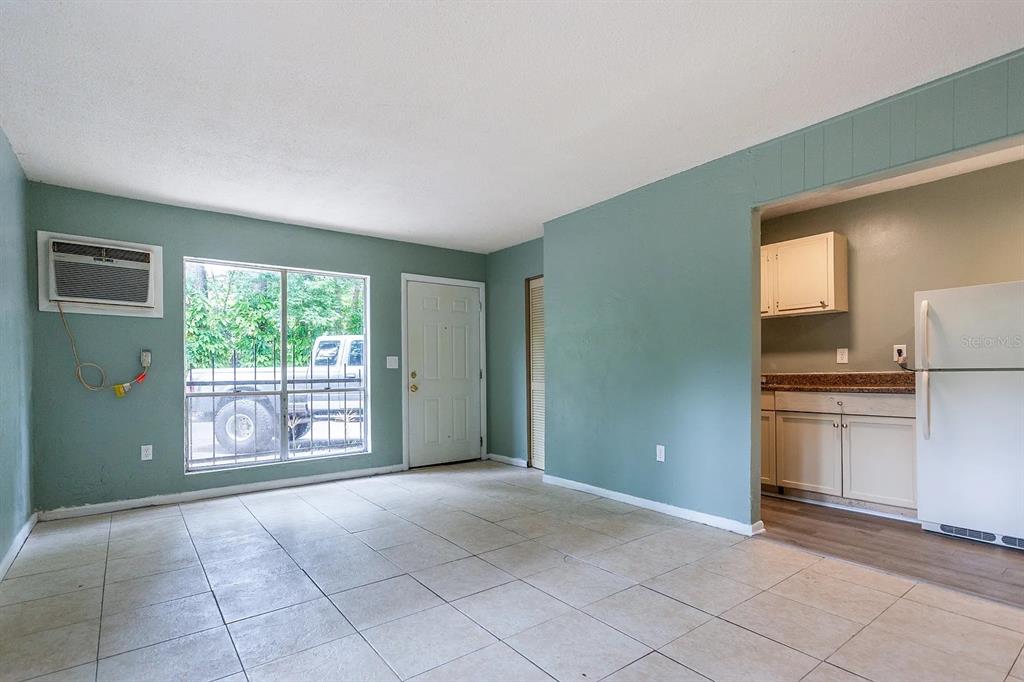 A living room with light-colored tile flooring, teal walls, and an adjacent kitchen area — 409 NE 11TH STREET, GAINESVILLE, FL