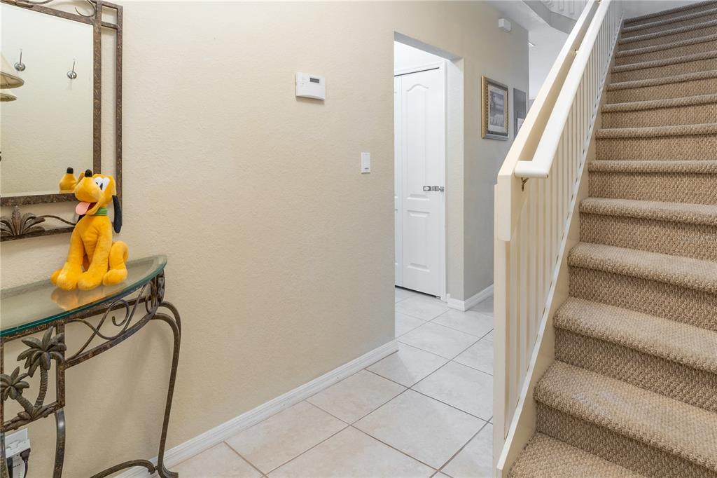 An entryway features a carpeted staircase, a glass-topped console table, and a tiled floor — 2457 CARAVELLE CIRCLE, KISSIMMEE, FL
