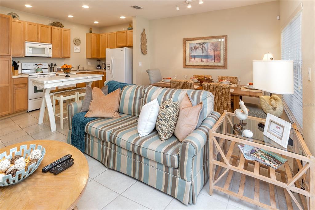 An open-concept living and dining area features a striped sofa, kitchen, and wooden furniture — 2457 CARAVELLE CIRCLE, KISSIMMEE, FL
