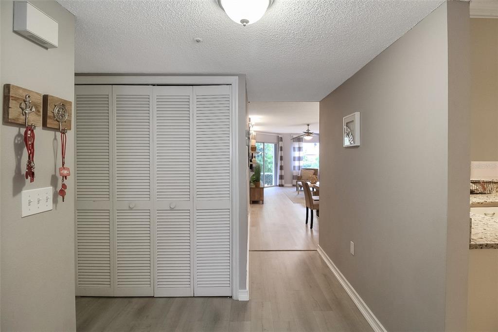 A hallway with light wood flooring leads to a living area with white louvered closet doors — 1326 SIESTA BAYSIDE DRIVE UNIT 1326-D, SARASOTA, FL
