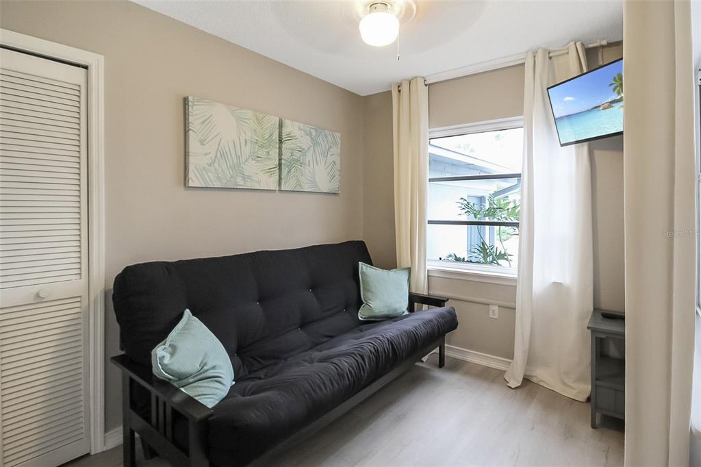 A small room features a black futon, light wood flooring, and a wall-mounted television — 1326 SIESTA BAYSIDE DRIVE UNIT 1326-D, SARASOTA, FL