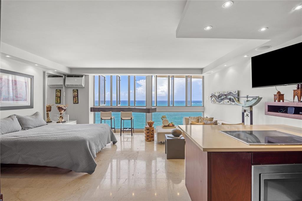 A studio apartment with a bed, kitchen island, and floor-to-ceiling windows overlooking the ocean — 1035 ASHFORD AVENUE UNIT 1206, SAN JUAN, PR