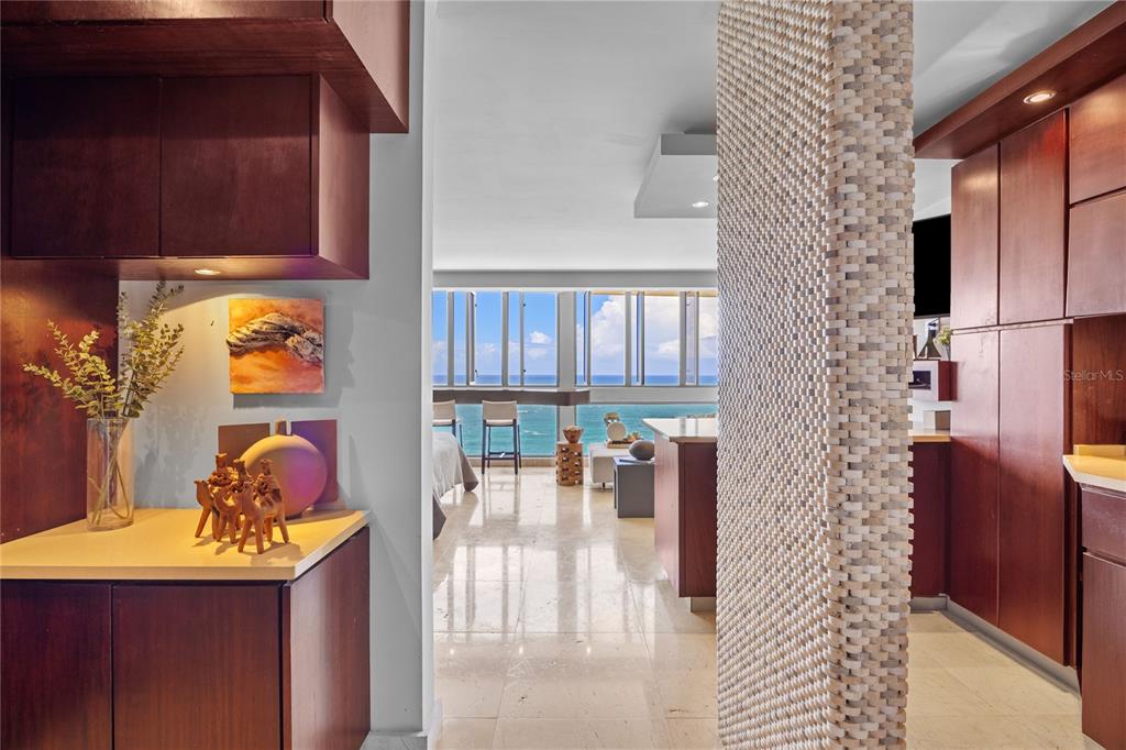 A view through a doorway shows a kitchen, living area, and oceanfront balcony — 1035 ASHFORD AVENUE UNIT 1206, SAN JUAN, PR