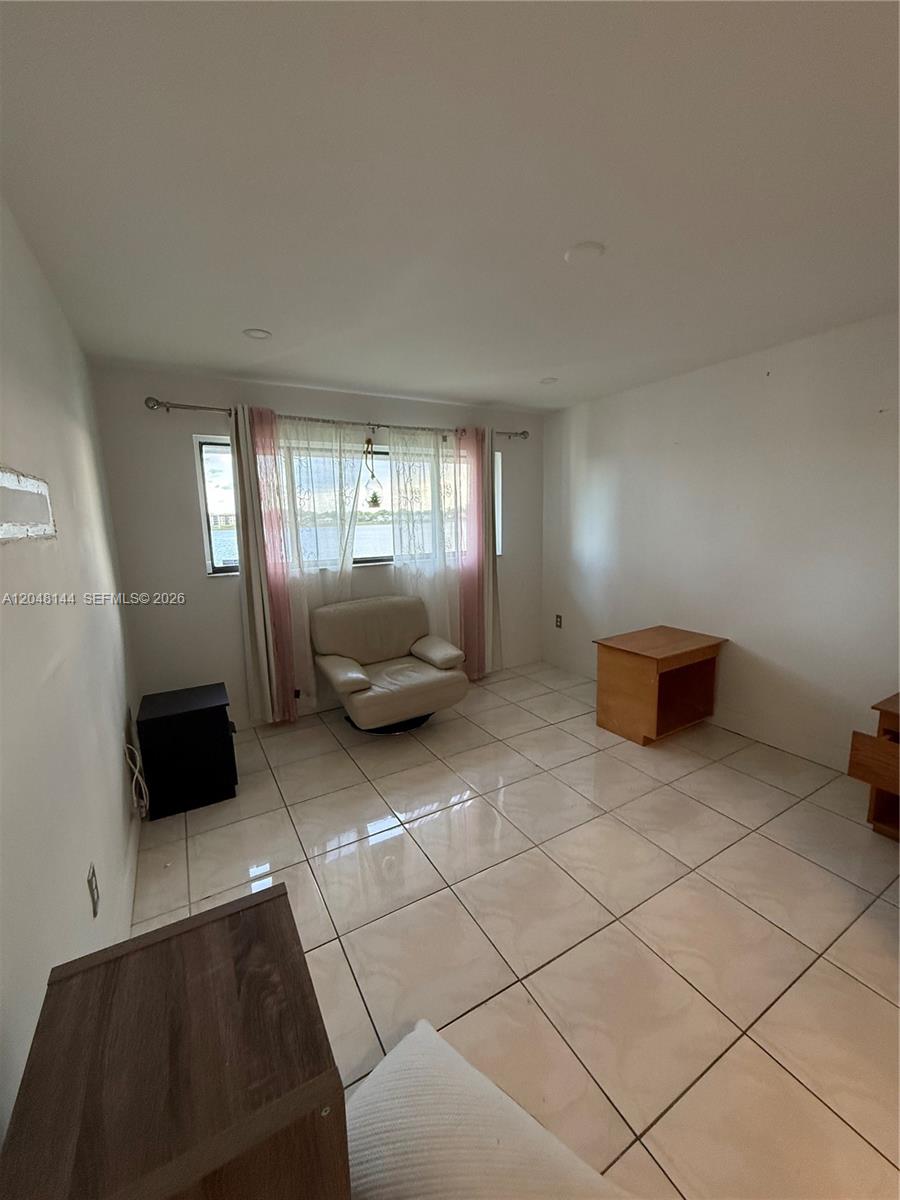A room with light-colored tile flooring, a single armchair, and a window overlooking water — 468 NE 206th Ln # 203, Miami FL 33179, MIAMI, FL