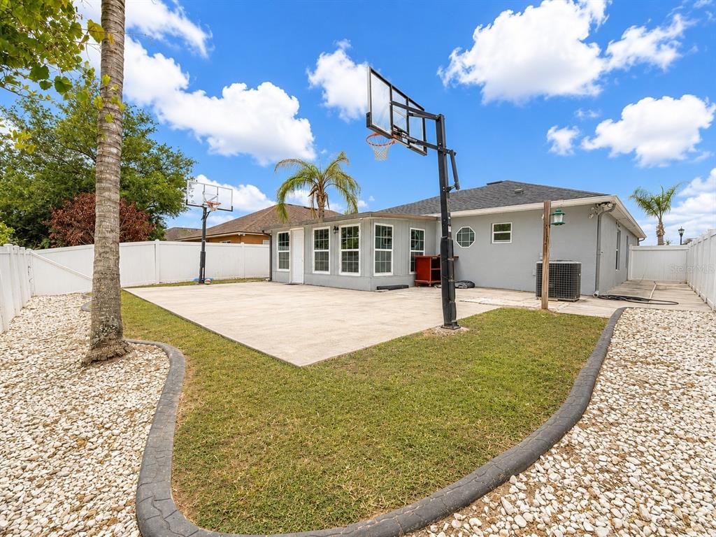 A backyard features a concrete basketball court, a gray house, and a white vinyl fence — 2221 PARIA LANE, KISSIMMEE, FL