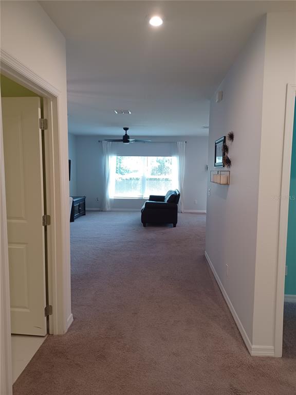 A view from a hallway looking into a carpeted living room with a large window — 14305 HIDDEN COURT, CLERMONT, FL