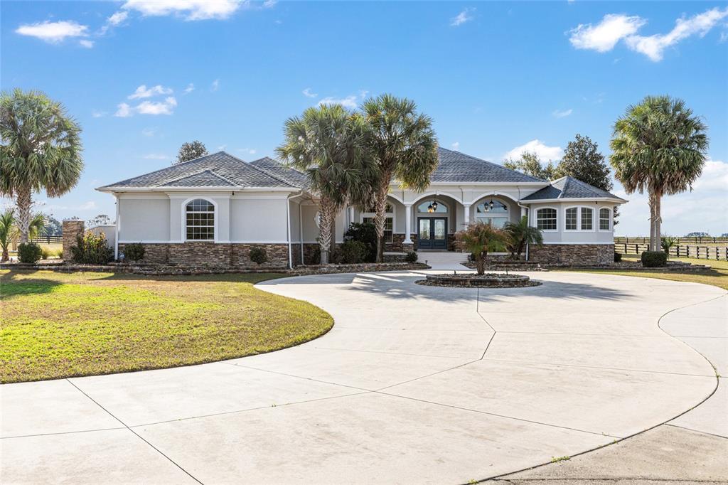 A single-story house with a stone facade, gray roof, and a large circular concrete driveway — 2655 NW 102ND BOULEVARD, WILDWOOD, FL