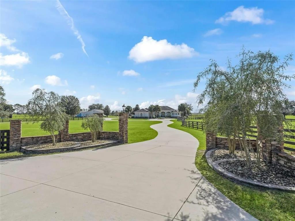 A concrete driveway leads through a stone-pillared entrance toward a house on a grassy lot — 2655 NW 102ND BOULEVARD, WILDWOOD, FL