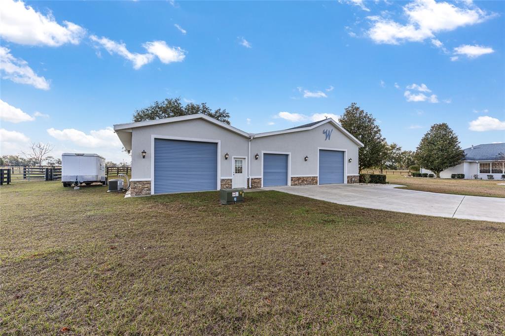 A light gray detached garage with three blue roll-up doors and stone accents — 2655 NW 102ND BOULEVARD, WILDWOOD, FL