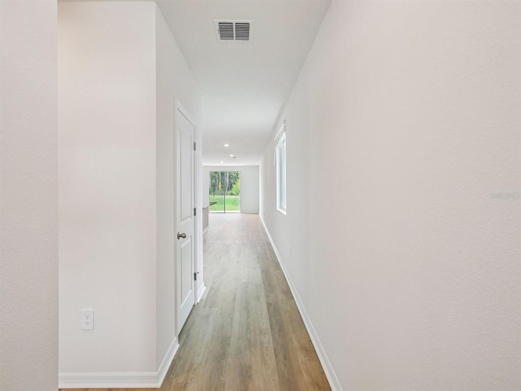 A hallway with light wood-look flooring leads toward a bright living area with sliding doors — 7488 MIA VINE DRIVE, BROOKSVILLE, FL