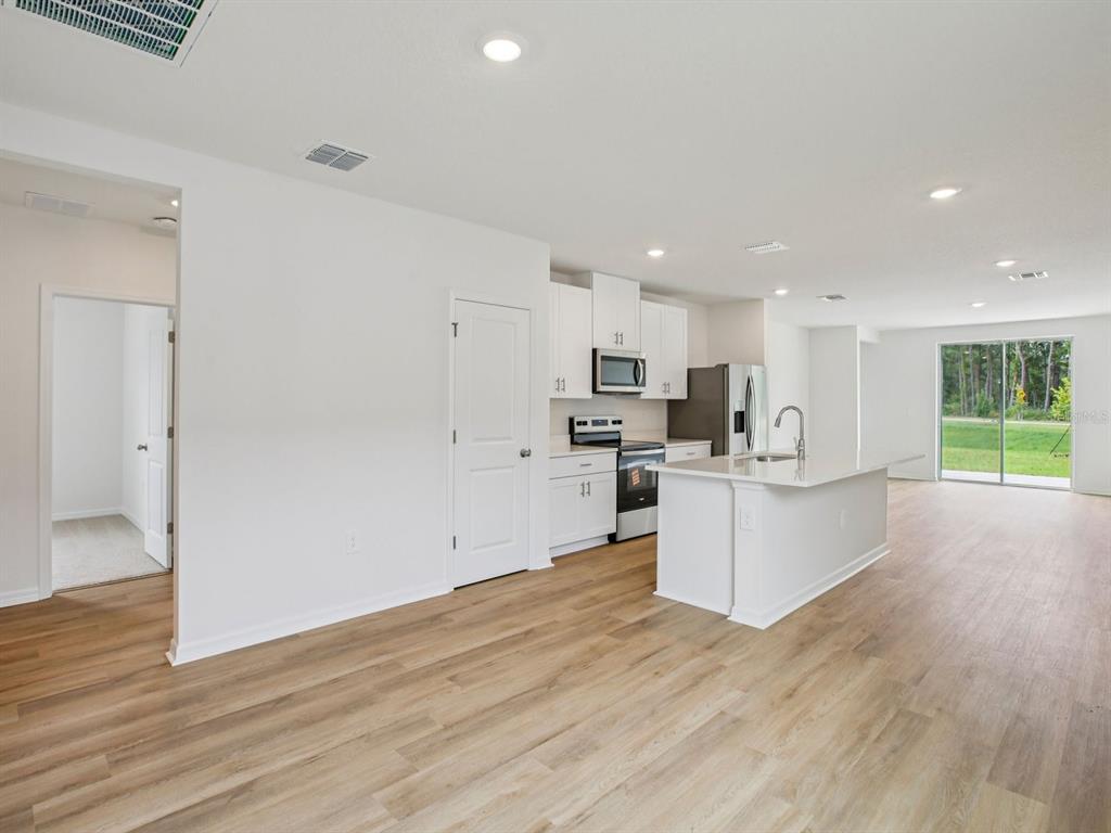 A modern kitchen with white cabinets and an island opens to a living area — 7488 MIA VINE DRIVE, BROOKSVILLE, FL