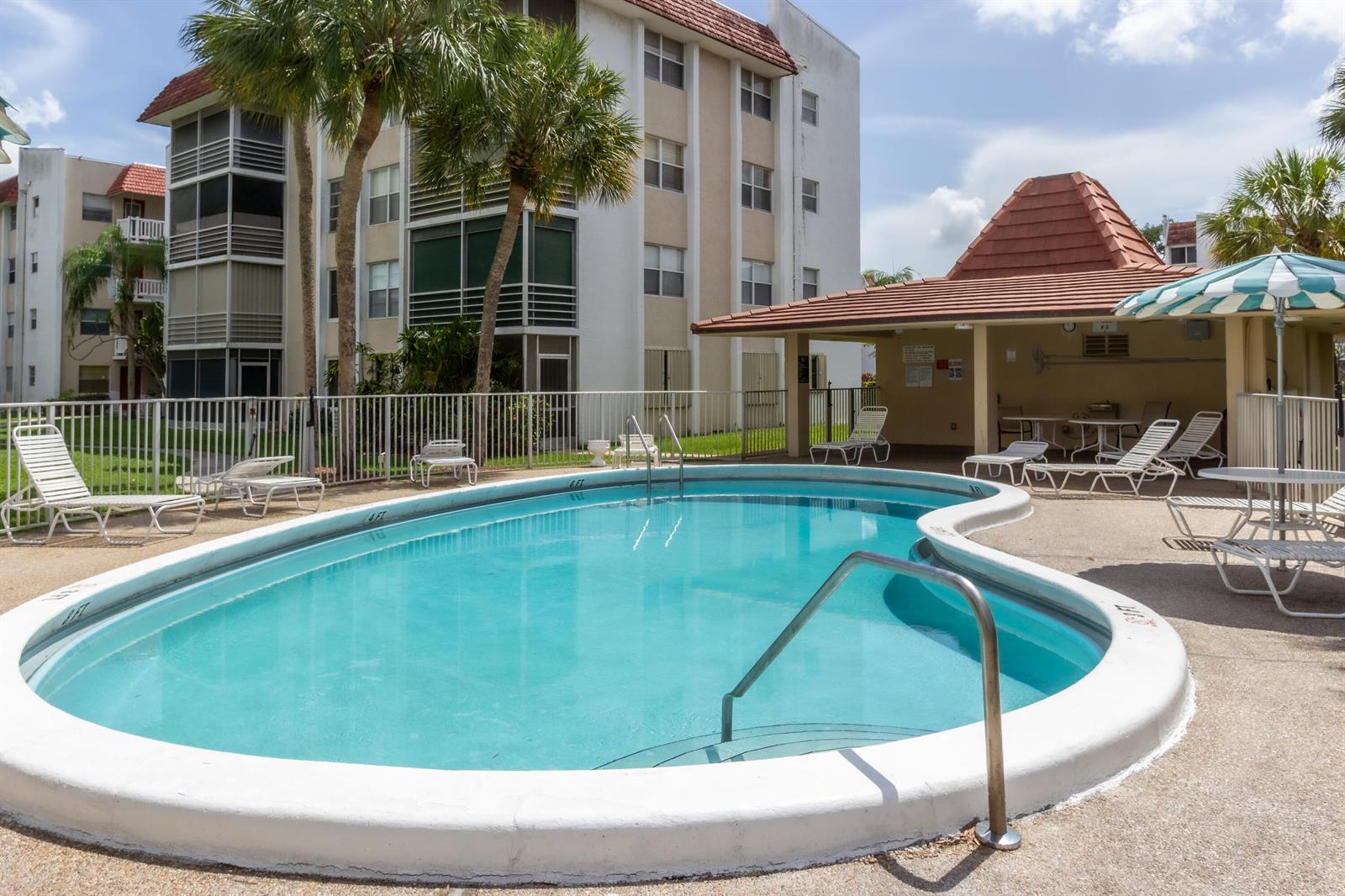 A kidney-shaped swimming pool sits in front of a multi-story apartment building and covered patio — 3531 Inverrary Drive # H406, Lauderhill FL 33319, LAUDERHILL, FL