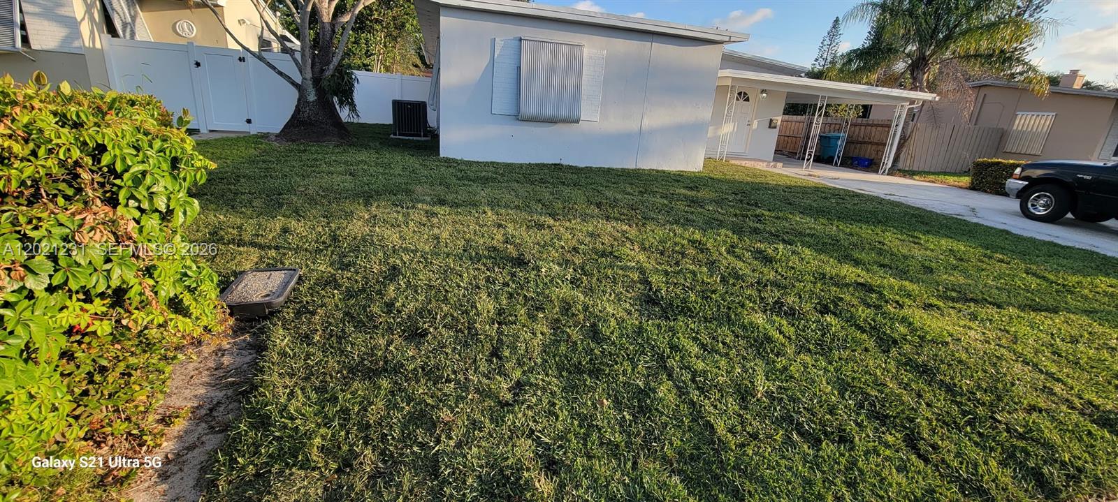 A view of a grassy front yard with a white house and a carport — 142 SE 4th ave, Boynton Beach FL 33435, BOYNTON BEACH, FL