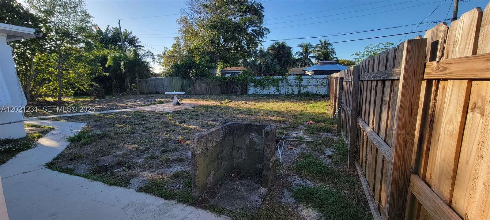 A backyard features a concrete patio, a small stone structure, and a wooden privacy fence — 142 SE 4th ave, Boynton Beach FL 33435, BOYNTON BEACH, FL