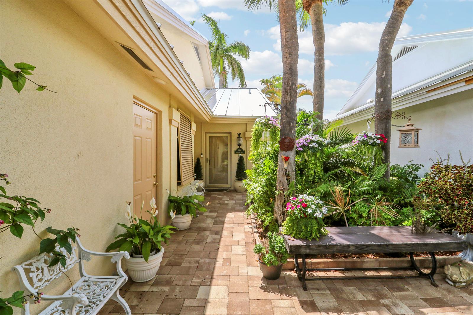 A paved walkway leads to a front door between two buildings with lush potted plants — 154 Sandbar Drive, Jupiter FL 33477, JUPITER, FL
